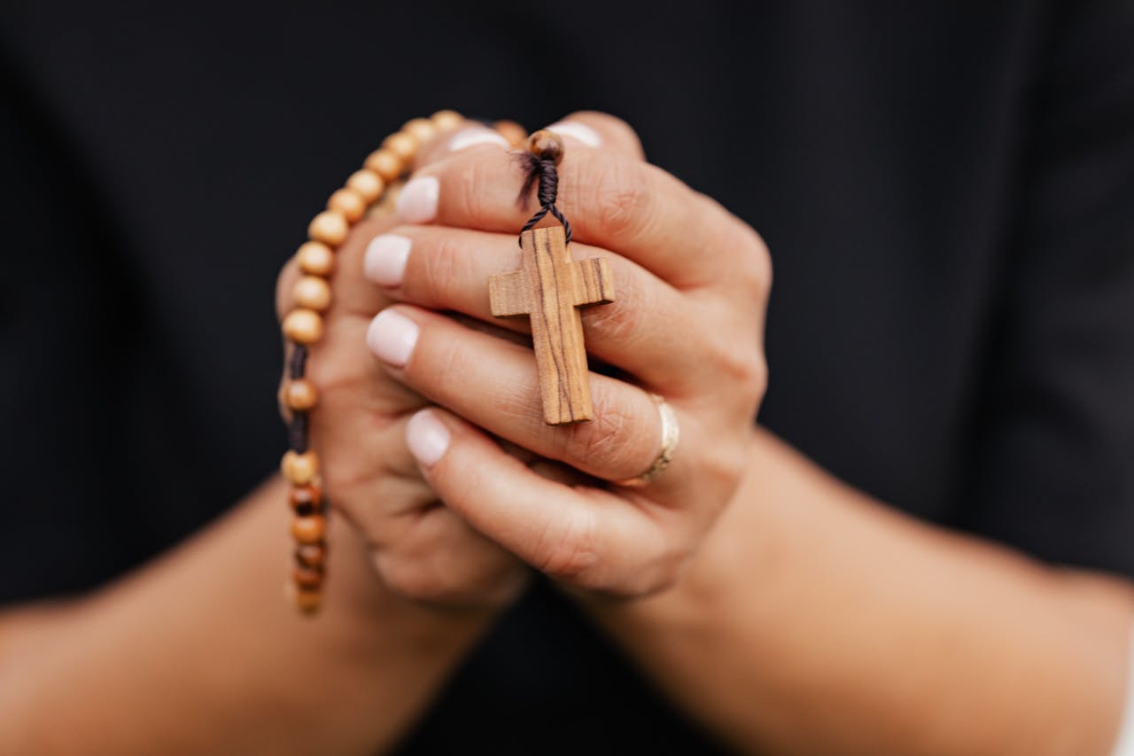 Home A detailed close-up of hands clasping a wooden rosary with cross, symbolizing faith.