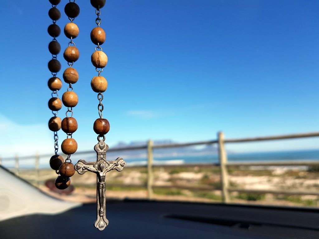 Mastering the First Impression: Your intriguing post title goes here A wooden rosary with a crucifix hangs inside a car, overlooking a scenic ocean view.