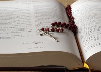 rosary-on-top-of-opened-bible-book-236339 Open Bible with red rosary beads draped on pages, symbolizing faith and devotion.