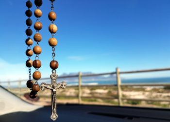 selective-focus-photo-of-brown-and-silver-rosary-208425 A wooden rosary with a crucifix hangs inside a car, overlooking a scenic ocean view.